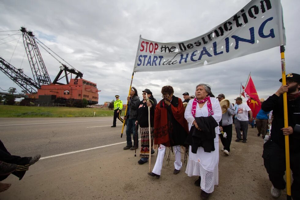 Menschen demonstrieren und halten ein Banner mit der Aufschrift "Stop the destruction, start the healing"
