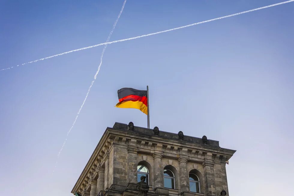 Deutschlandflagge am Reichstagsgebaeude in Berlin, 24.02.2025 Ein Gebäudeturm des Reichstags in Berlin mit wehender deutscher Flagge. Am Himmel kreuzen sich zwei Kondensstreifen.